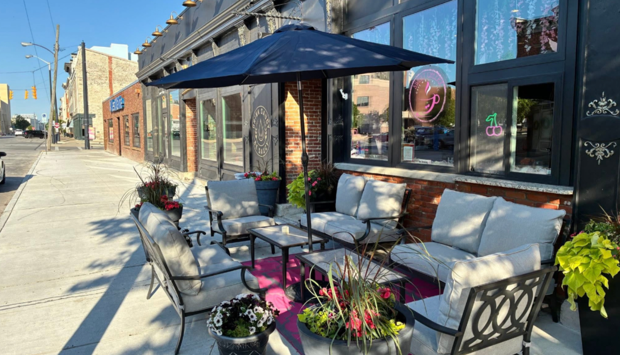 Outdoor patio at Sweet Cheekz Café N’ Bistro with pink flowers and lounge seating under an umbrella